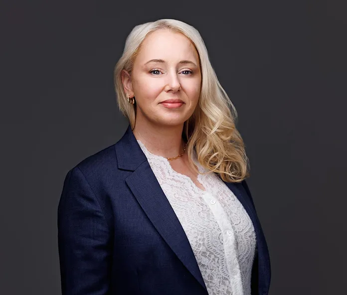 Professional portrait of a blonde woman wearing a navy blazer and white lace blouse.